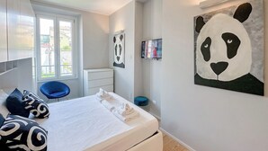 Une chambre à coucher moderne avec un lit, une chaise bleue, une commode blanche et une grande œuvre d’art représentant un panda accrochée au mur.