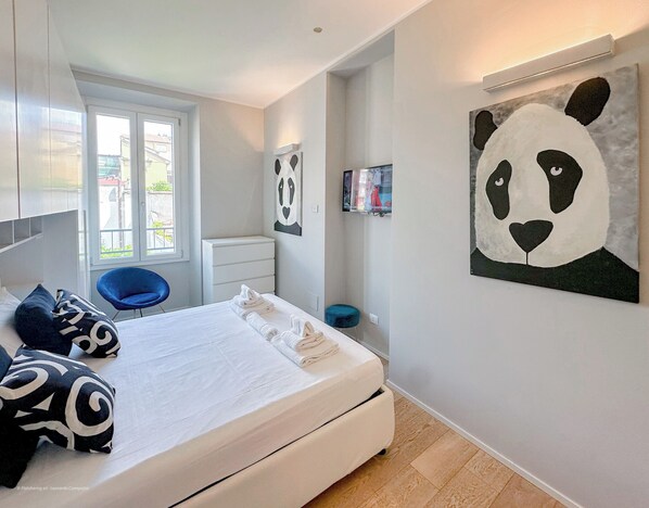Un dormitorio moderno con una cama, una silla azul, un tocador blanco y una gran obra de arte de un panda en la pared.