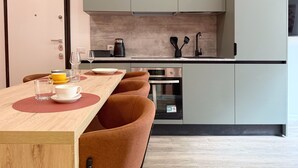 A modern kitchen with grey cabinets, a wooden dining table with orange chairs, and a coffee maker on the counter.