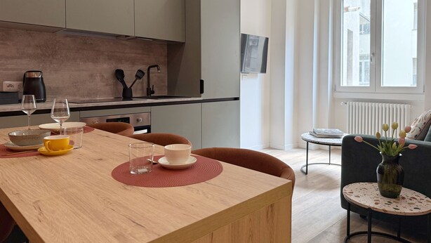 A modern kitchen with a dining area, a coffee machine, and a view of the city through large windows.