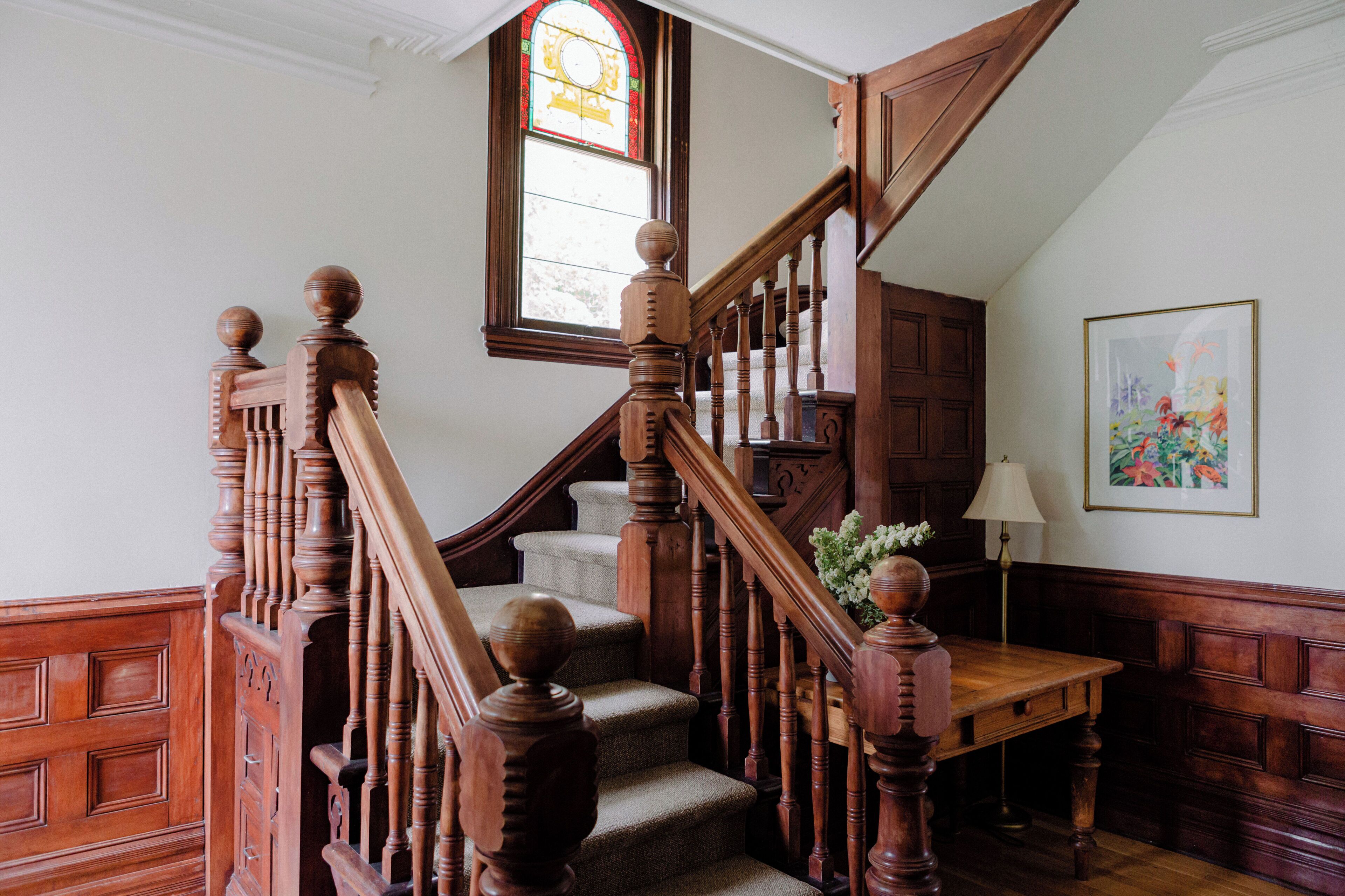 Un escalier en bois avec une rampe, une petite table et une lampe fixée au mur.