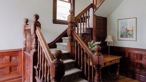 A wooden staircase with a handrail, a small table, and a wall-mounted lamp. - Bayview House at Lake on the Mountain (Prince Edward)