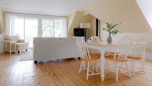 A spacious living room with a sofa, a dining table with chairs, and a large window providing natural light. - Bayview House at Lake on the Mountain (Prince Edward)