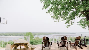 Une terrasse en bois avec une table de pique-nique et des fauteuils Adirondack, donnant sur une étendue d’eau.