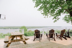 Una terraza de madera con una mesa de picnic y sillas Adirondack con vista al agua.
