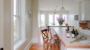 A kitchen with a central island, wooden chairs, a dining table, pendant lights, and a view of the outdoors through large windows. - Bayview House at Lake on the Mountain (Prince Edward)