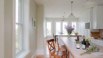 Une cuisine dotée d’un îlot central, de chaises en bois, d’une table à manger, de luminaires suspendus et offrant une vue sur l’extérieur grâce à de grandes fenêtres.