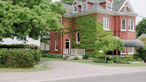 A large, red brick house with a prominent front porch and a covered porch area. - Bayview House at Lake on the Mountain (Prince Edward)