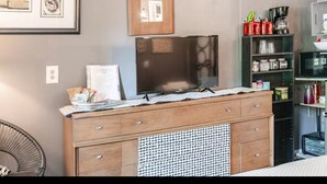 Una cocina con un armario de madera, microondas y refrigerador. Hay un cuadro en la pared y una silla en la esquina.