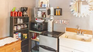 Cocina compacta con refrigerador, microondas y lavaplatos. Hay repisas con diversos utensilios de cocina y un cartel que dice 'PEACE'.