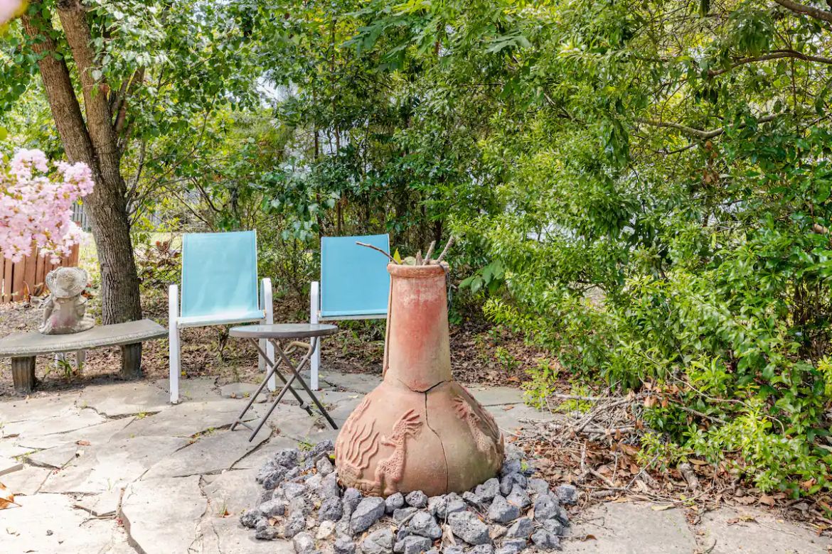 Ein Gartenbereich mit einem Terrakottatopf, zwei blauen Klappstühlen und einer Steinbank.