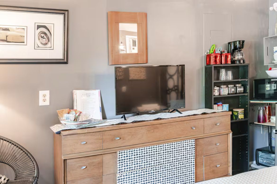 Une cuisine avec des meubles de rangement en bois, un four à micro-ondes et un réfrigérateur. Un tableau encadré est accroché au mur et une chaise se trouve dans un coin.