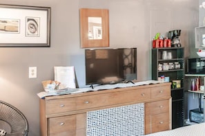 Una cocina con un armario de madera, microondas y refrigerador. Hay un cuadro en la pared y una silla en la esquina.