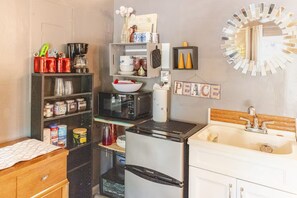 Cocina compacta con refrigerador, microondas y lavaplatos. Hay repisas con diversos utensilios de cocina y un cartel que dice 'PEACE'.