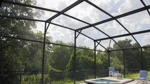 A covered outdoor swimming pool with a view of trees and a clear sky.