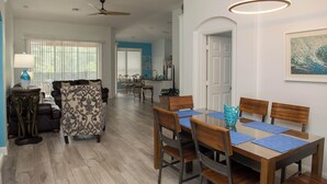 A spacious living area with a dining table set for four, a sofa, and a ceiling fan.