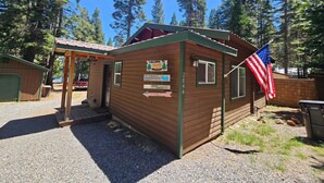 A small wooden cabin with a welcome sign, an American flag, and a sign indicating a nearby campground.