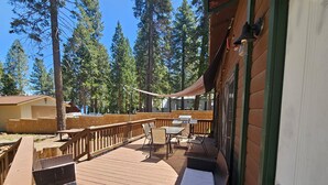 A wooden deck with outdoor furniture, a barbecue grill, and a view of tall trees.