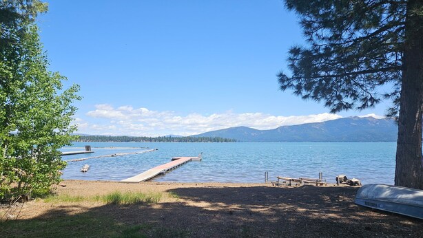 A lakeside view with a dock extending into the water, surrounded by trees and a clear sky.