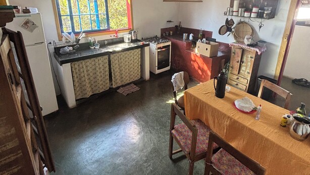 A compact kitchen with a window, a sink, a stove, and a dining table with chairs. - Pousada Casa Matriz (Itabirito)