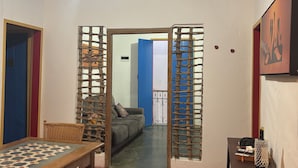 A room with a dining table, chairs, a sofa, and a small table with a decorative item. There is a doorway leading to another room with a blue door and a balcony. - Pousada Casa Matriz (Itabirito)