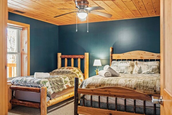 A bedroom with two wooden beds, a ceiling fan, and a window with a view of trees.