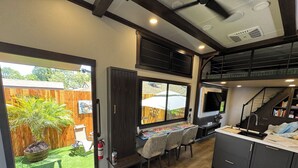 A compact kitchen with a dining area, a built-in TV, and a staircase leading to a loft.