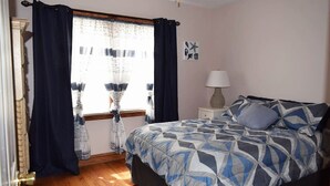 Un dormitorio con cama, cortinas, una ventana, lámpara y alfombra.