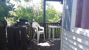 Una terraza de madera con una silla de plástico blanca y un banco, que da a un porche cubierto.