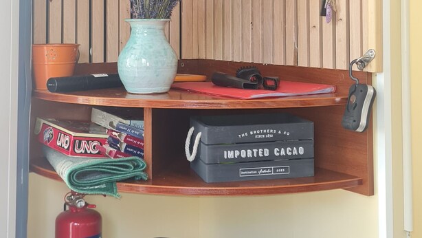 Una habitación con paneles de madera, un televisor montado y estantes con libros, un jarrón y un extintor.