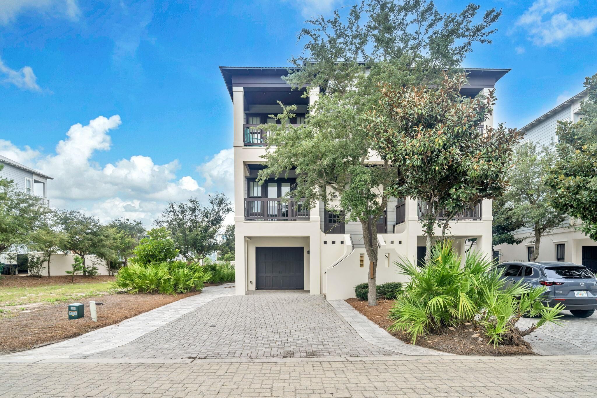 A modern multi-story residential building with a paved driveway and landscaped garden.