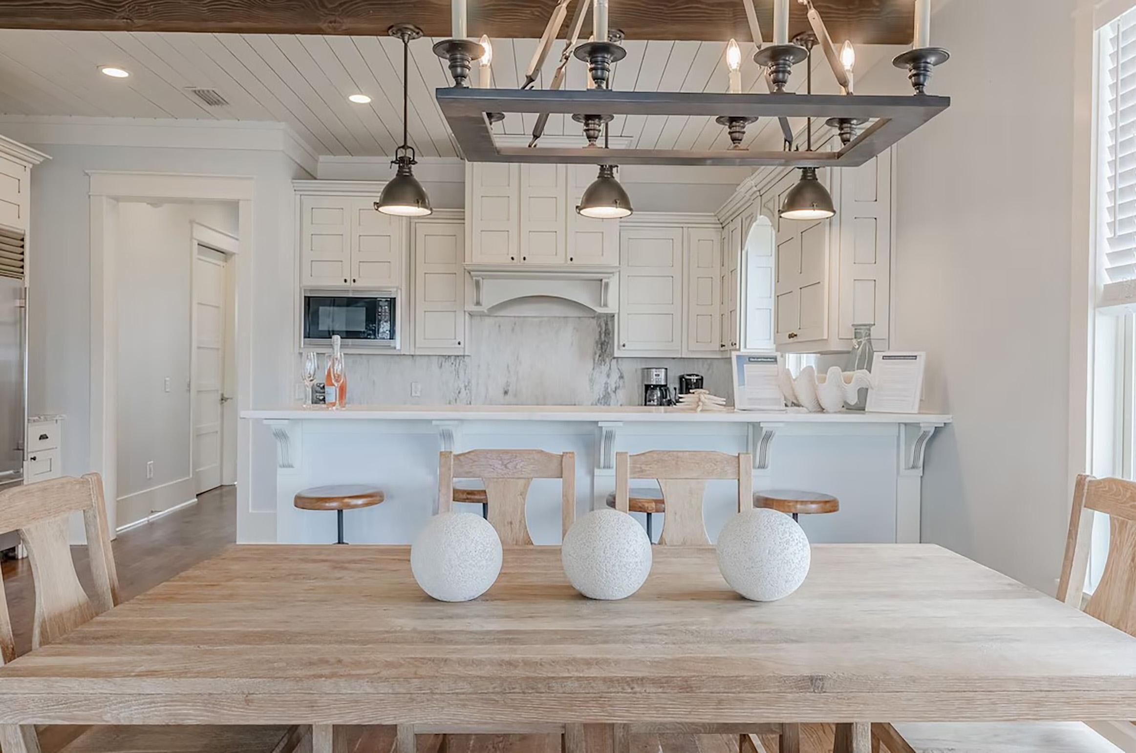 Una cocina moderna con armarios blancos, una isla de mármol y una mesa de comedor de madera con tres taburetes redondos.