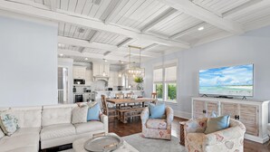 A spacious living area with a large TV, a dining table, and a kitchen in the background. - Inlet Beach Retreat 202 (Panama City Beach)