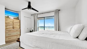 Una camera da letto con un letto, una ventola a soffitto, vista sulla spiaggia e un'armadiatura in legno.