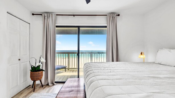 Una camera da letto con un letto grande, un comodino, una lampada, una finestra vista spiaggia e una porta.