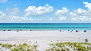 Una spiaggia con sabbia bianca, acqua cristallina e alcuni ombrelloni e tende.