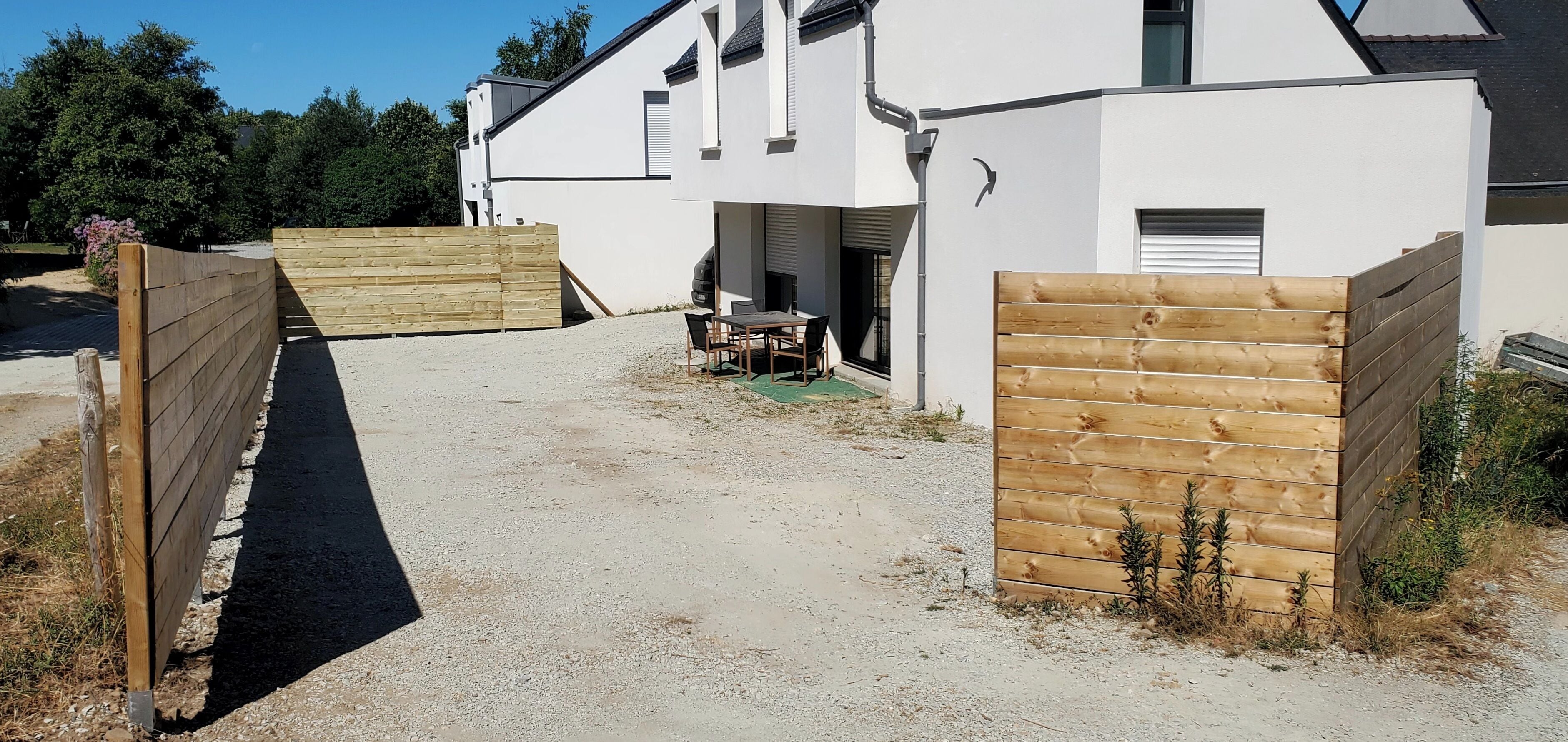 A modern two-story building with a gravel driveway and wooden gates.