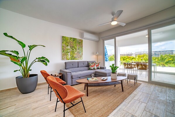 A modern living room with a grey sofa, orange armchairs, a coffee table, and a large potted plant.