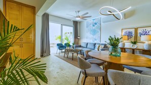 A modern living room with a sofa, chairs, a dining table, and a ceiling fan. - Cana Brava Residences - Elite Apartment, Golf View (Punta Cana)