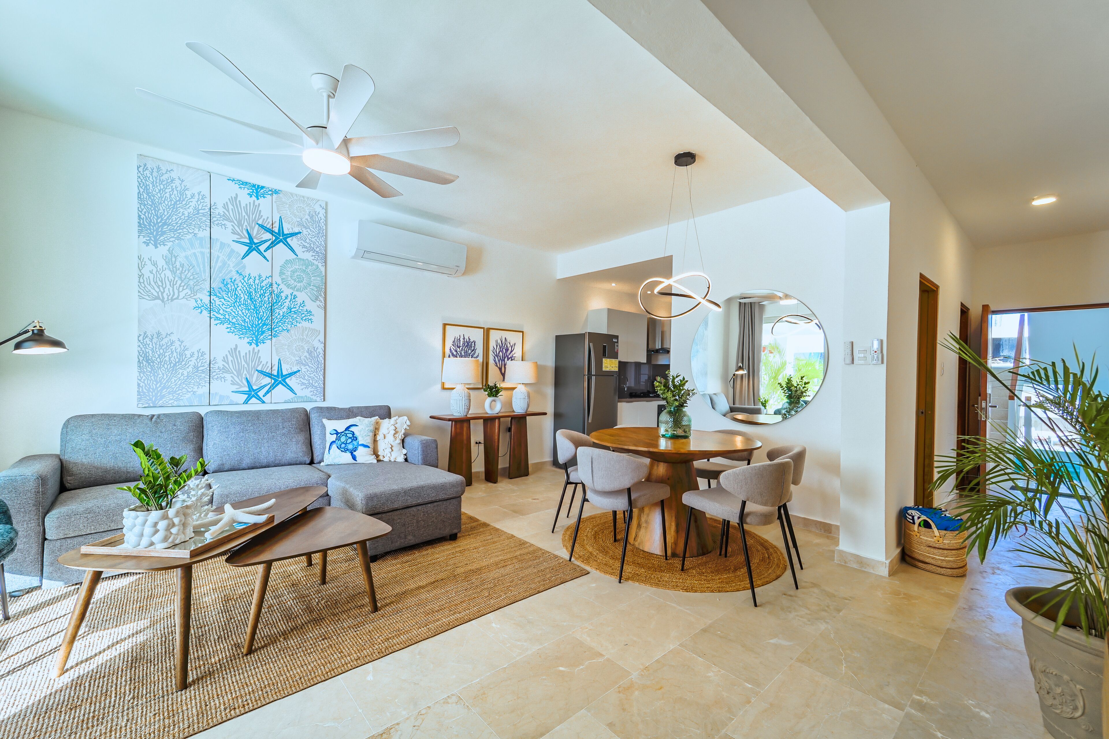 Uma sala de estar moderna com um sofá cinzento, uma mesa de centro de madeira e uma área de jantar com uma mesa redonda e cadeiras.