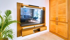 A modern living room with a large flat-screen TV mounted on a wooden wall unit, a comfortable seating area with a sofa and coffee table, and a wooden wardrobe. - Cana Brava Residences - Elite Apartment, Golf View (Punta Cana)