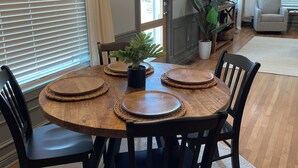 Un coin repas avec une table ronde en bois, des chaises noires, des sets de table en fibres tressées et une plante en pot.