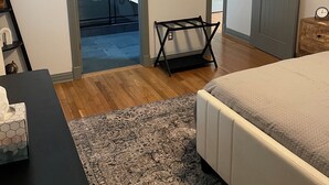 Une chambre à coucher comprenant un lit, une petite table, une chaise, un tapis et une porte donnant sur une salle de bain.