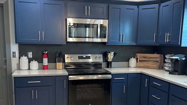 Une cuisine moderne avec des meubles bleu foncé, des appareils en acier inoxydable et un plancher en bois.