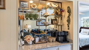 A hotel room with a glass display case filled with decorative items, a coffee maker, and a bed with a "SAND" pillow. - The Bent Rod-Charming Canal home! (Jamaica Beach)