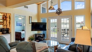 A spacious living room with a large TV, comfortable seating, and a view of the outdoors through a sliding glass door. - The Bent Rod-Charming Canal home! (Jamaica Beach)
