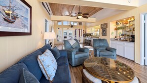 A spacious living area with a high ceiling, a ceiling fan, and a kitchen in the background. - The Bent Rod-Charming Canal home! (Jamaica Beach)