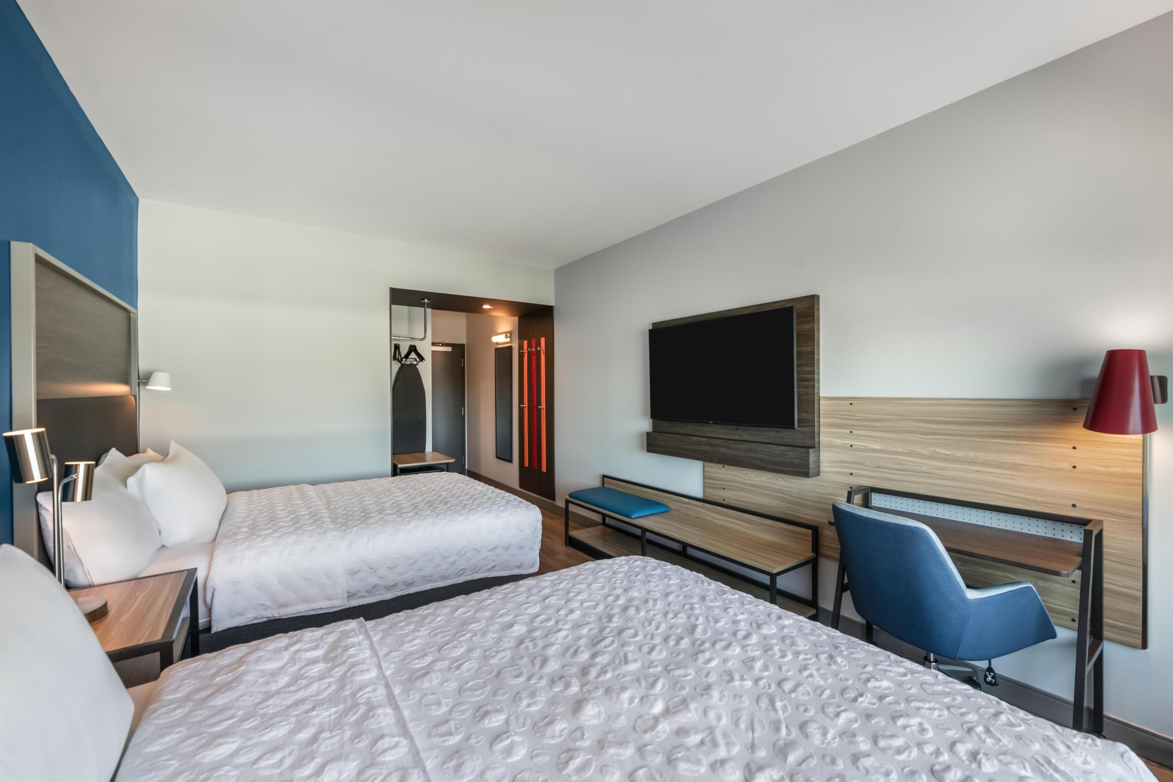 Une chambre d’hôtel avec deux lits, une télévision, un bureau, une chaise et une lampe.