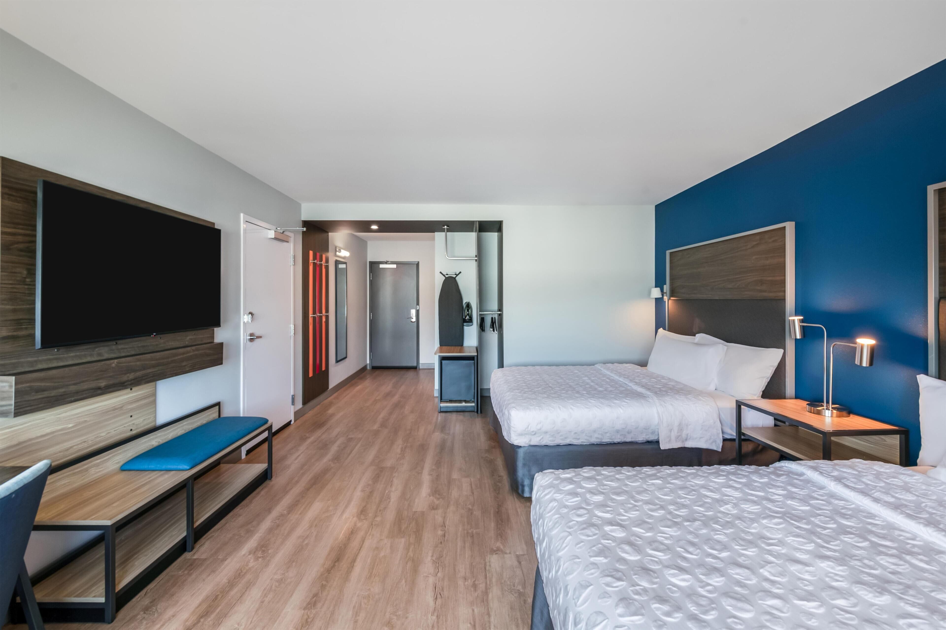 A hotel room with two beds, a desk, a TV, and a small table with lamps.