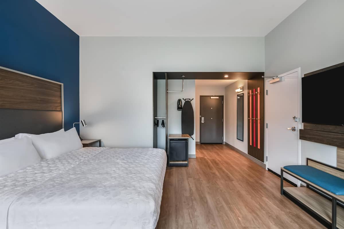 A modern hotel room with a large bed, a desk, a TV, and a bathroom visible through an open door.